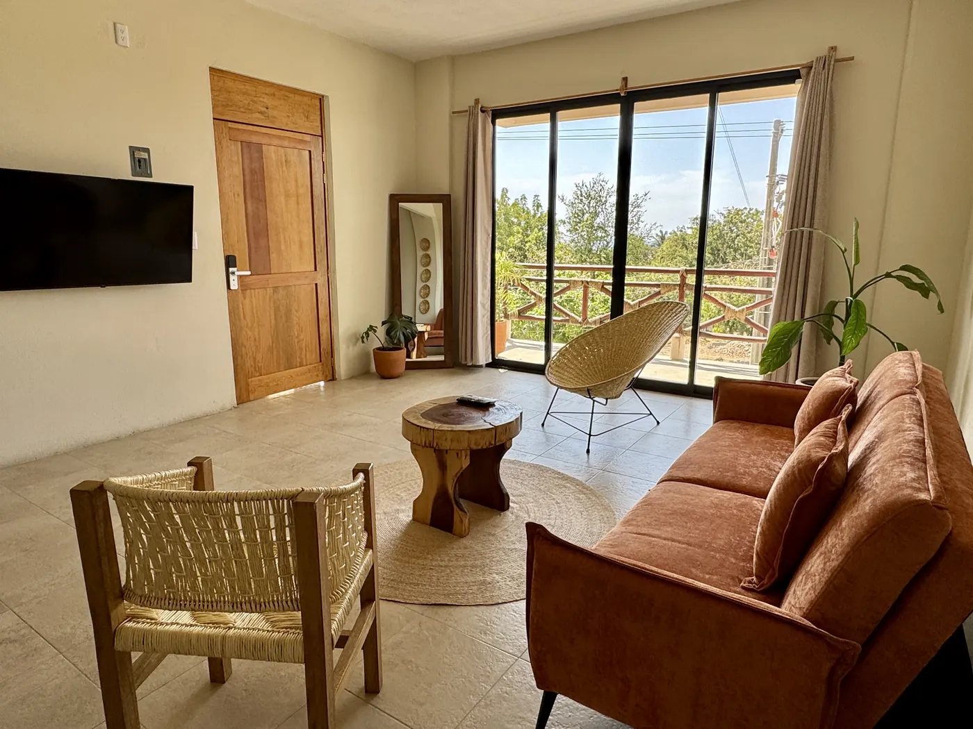 Sala con sofá de terciopelo terracota, sillas tejidas y ventanal