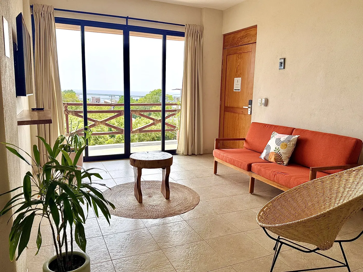 Sala con sofá terracota, silla tejida y ventanal al balcón